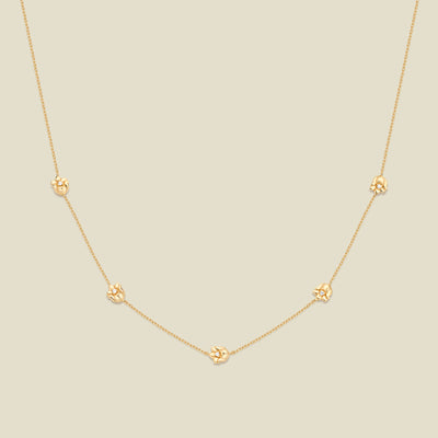 A delicate gold chain necklace featuring five small, evenly spaced textured lily of the valley flower motifs set with tiny clear stones, displayed on a solid light beige background.