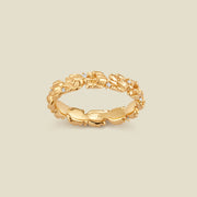 A gold floral-etched ring band with textured lily of the valley flowers and small clear gemstones, shown on a plain warm beige background. 