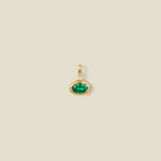 A gold oval pendant charm with a green bezel-set oval gemstone and a clear accent stone on top, set against a solid beige background.