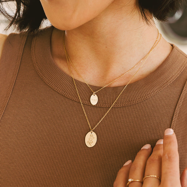 A close-up of a person wearing a layered gold necklace set with two oval pendant chains over a brown ribbed top.