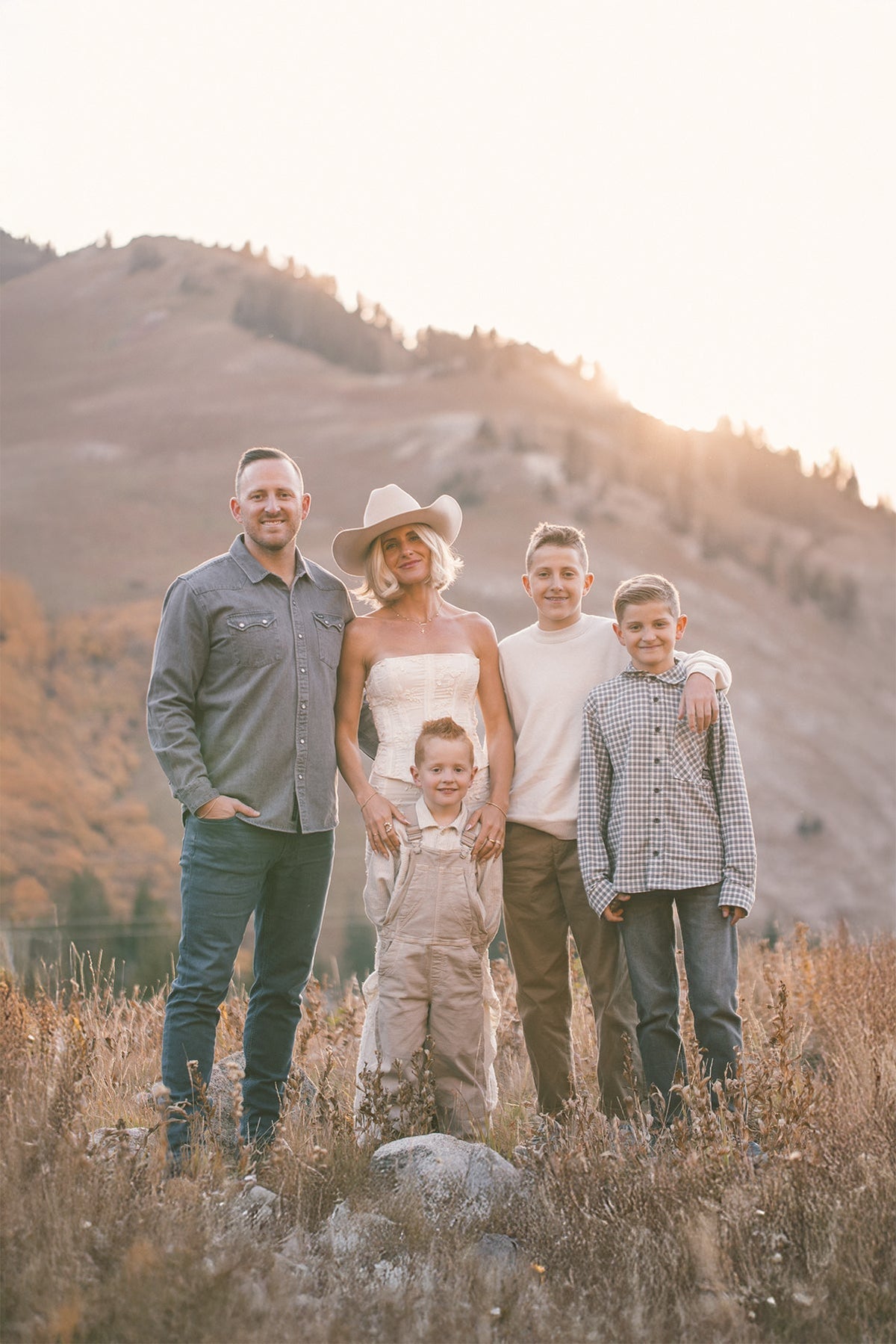 A family in corresponding neutral clothing, standing in a beige toned field with a mountain in the background.