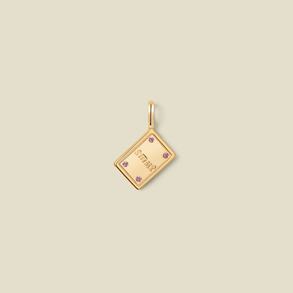 A gold book pendant charm with the word 'SMUT' engraved in the center and four pink accent stones on the corners.