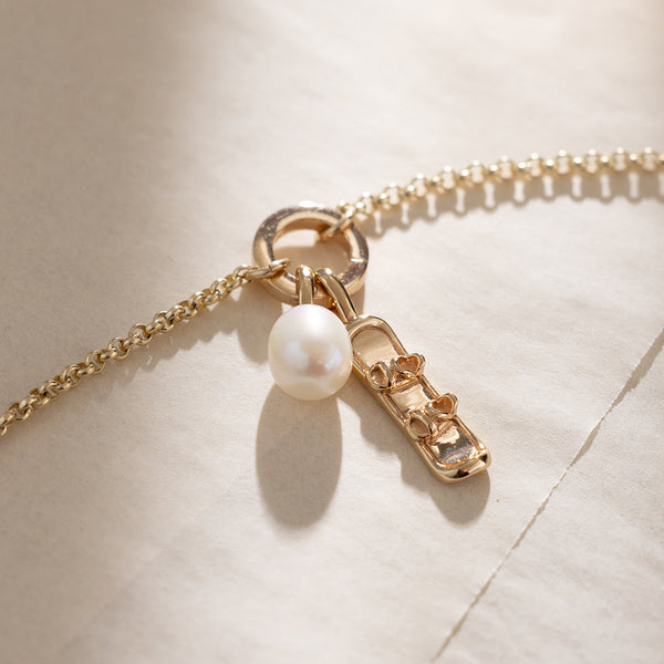 Gold necklace with a pearl and snowboard charm on a beige background