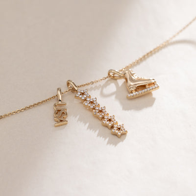 A gold dainty chain necklace featuring a 'USA' charm, a vertical stacking star charm with clear stones, and a figure skate charm.