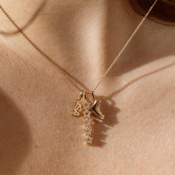 A close up lifestyle shot of a person's neck with a gold dainty chain necklace featuring a 'USA' charm, a vertical stacking star charm with clear stones, and a figure skate charm.