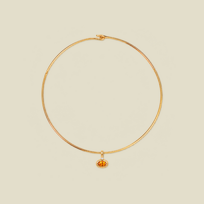 A thin gold wire choker necklace with a small oval amber gemstone pendant, displayed on a solid light beige background.