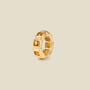 A gold ring charm with multiple bezel set square-cut amber gemstones set side by side to create the band, shown on a solid beige background.