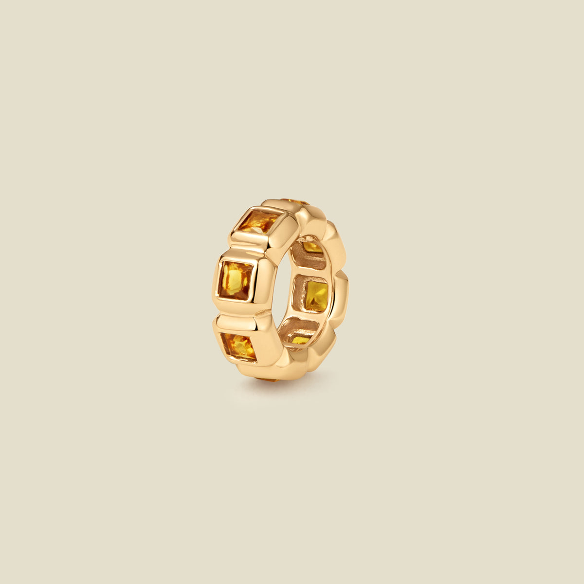 A gold ring charm with multiple bezel set square-cut amber gemstones set side by side to create the band, shown on a solid beige background.