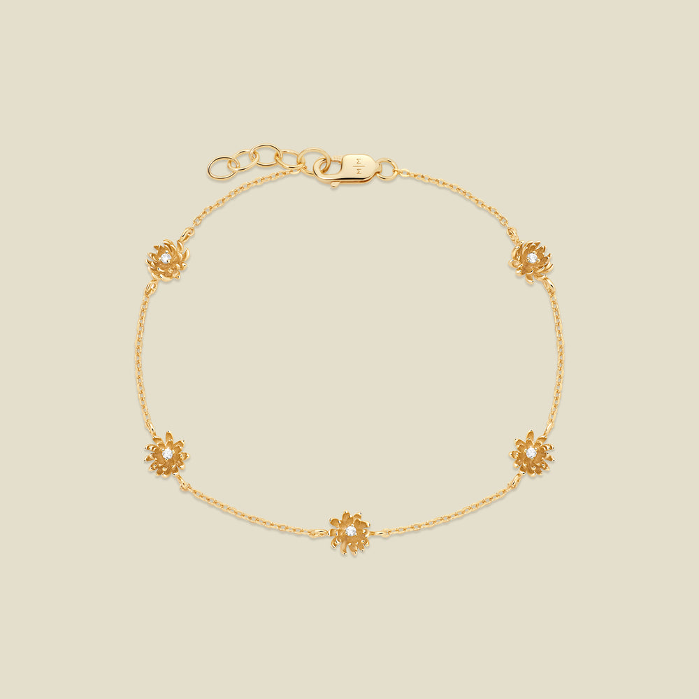 A delicate gold chain bracelet with five small chrysanthemum flower charms, each set with a clear round stone, displayed on a light beige background.