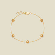 A delicate gold chain bracelet with five small chrysanthemum flower charms, each set with a clear round stone, displayed on a light beige background.