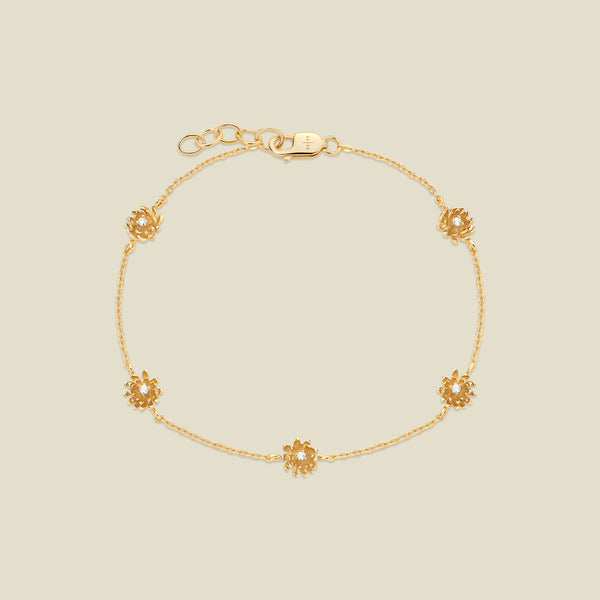 A delicate gold chain bracelet with five small chrysanthemum flower charms, each set with a clear round stone, displayed on a light beige background.