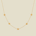 A delicate gold chain necklace featuring five small, evenly spaced textured chrysanthemum flower motifs set with tiny clear stones, displayed on a solid light beige background.