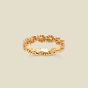 A gold floral-etched ring band with textured chrysanthemum flowers and small clear gemstones, shown on a plain warm beige background. 
