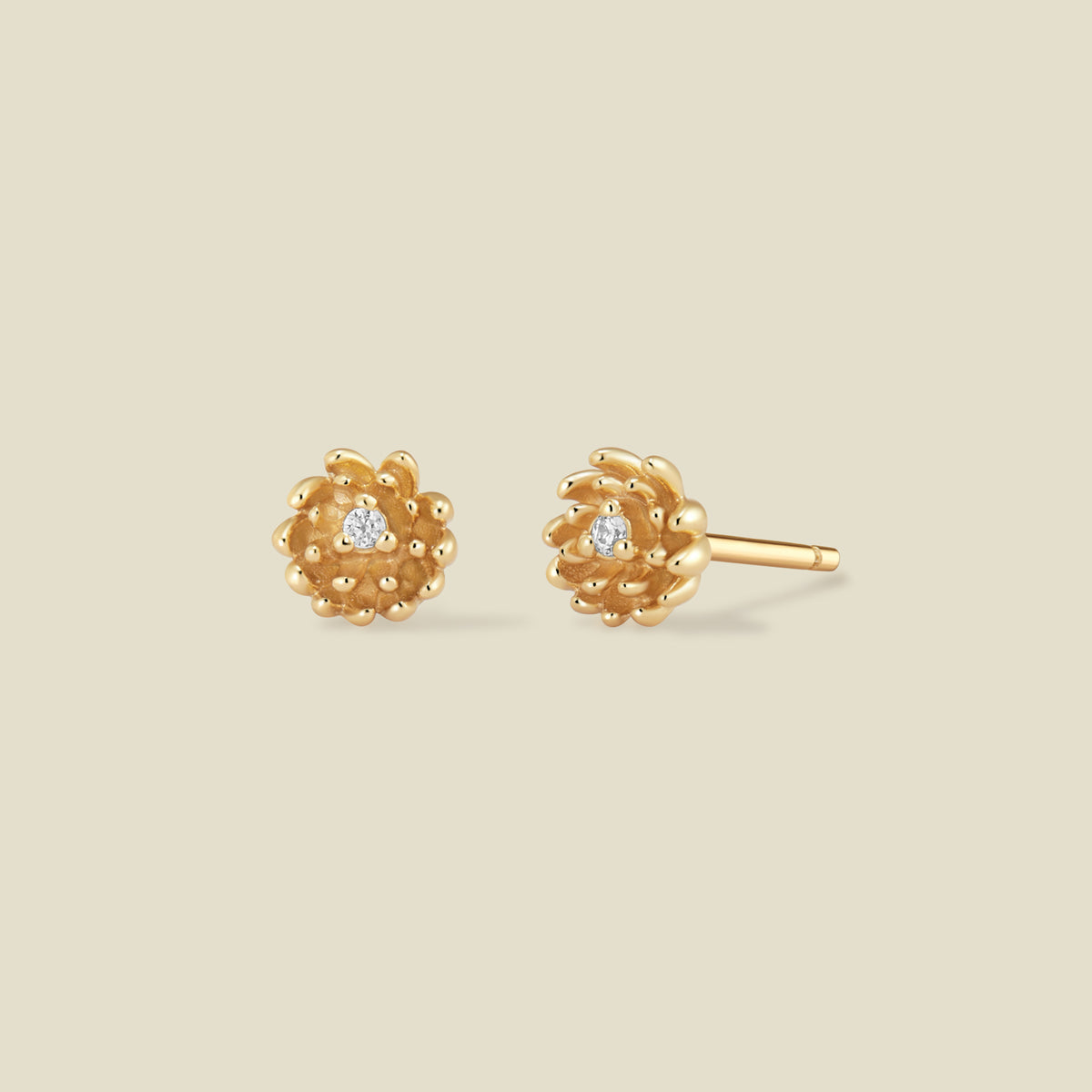 A pair of gold chrysanthemum flower stud earrings, each featuring a small round clear gemstone at the center, displayed on a solid light beige background.
