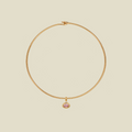 A delicate gold wire hoop necklace with a small oval-shaped pink gemstone pendant, displayed on a solid light beige background.