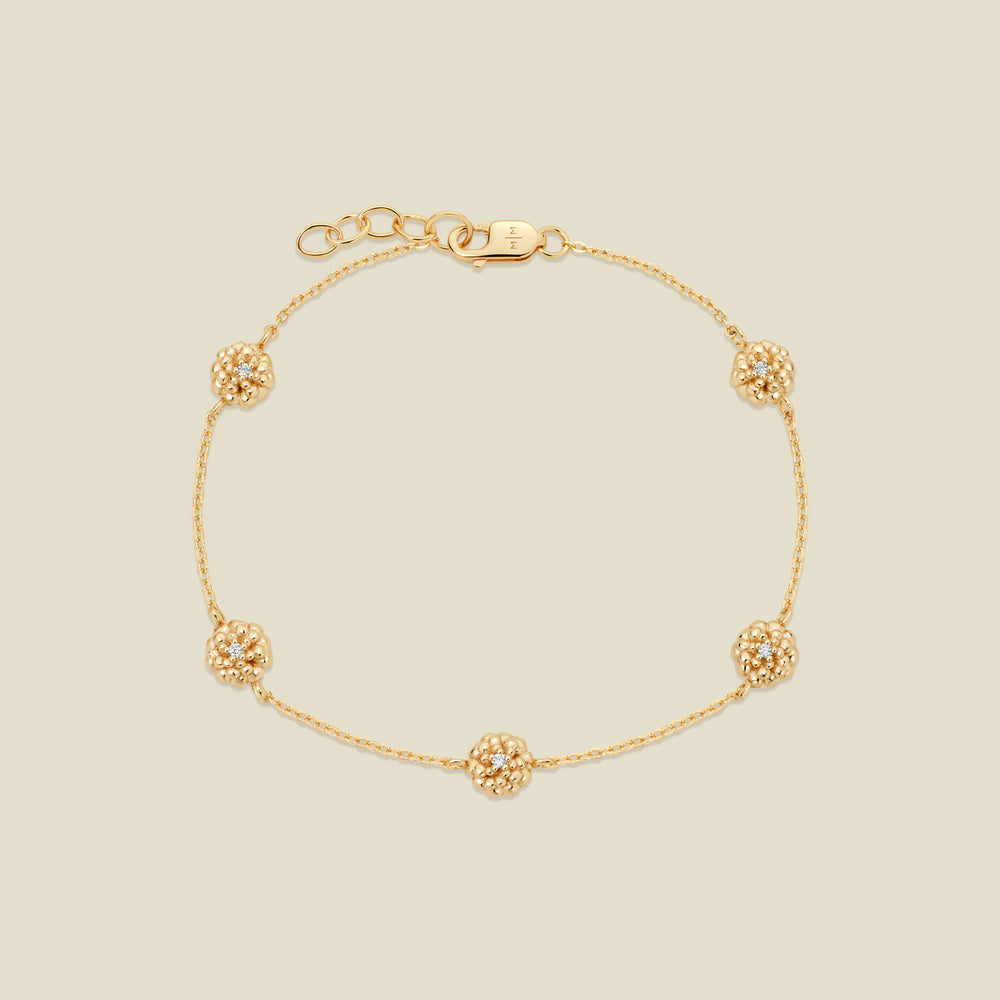A delicate gold chain bracelet featuring five ornate, textured gold marigold charms with small clear stones, arranged in a circle on a light beige background.