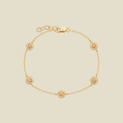 A delicate gold chain bracelet featuring five ornate, textured gold marigold charms with small clear stones, arranged in a circle on a light beige background.