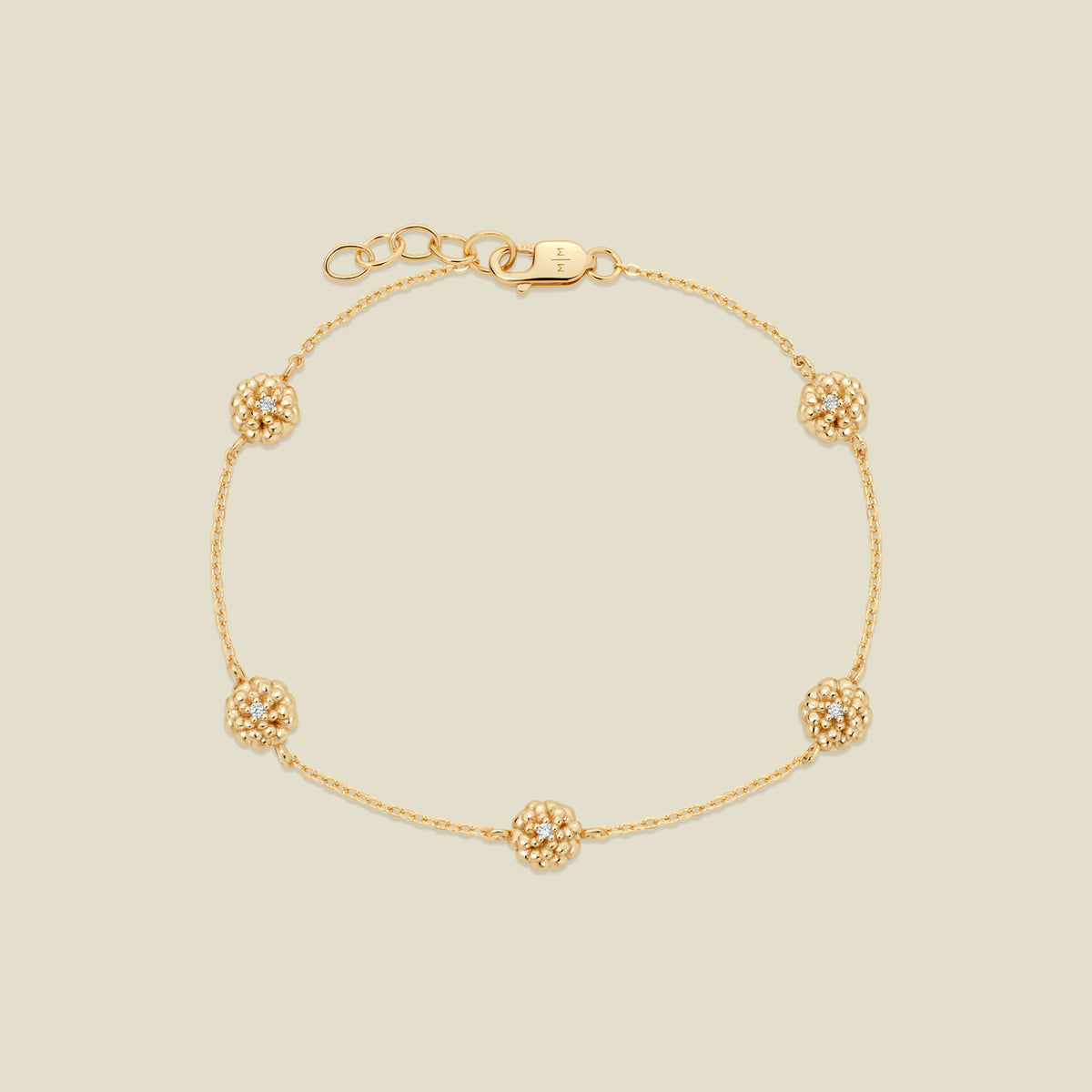 A delicate gold chain bracelet featuring five ornate, textured gold marigold charms with small clear stones, arranged in a circle on a light beige background.