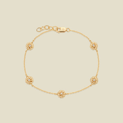 A delicate gold chain bracelet featuring five ornate, textured gold marigold charms with small clear stones, arranged in a circle on a light beige background.