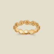 A gold floral-etched ring band with textured marigold flowers and small clear gemstones, shown on a plain warm beige background. 