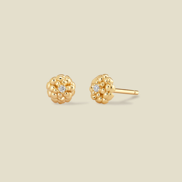A pair of gold stud earrings with a textured, marigold flower-like cluster design and a small clear gemstone in the center of each, shown on a solid light beige background.