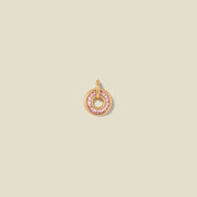 A circular gold pendant featuring pink baguette-cut stones around a hollow center, displayed against a solid light beige background.