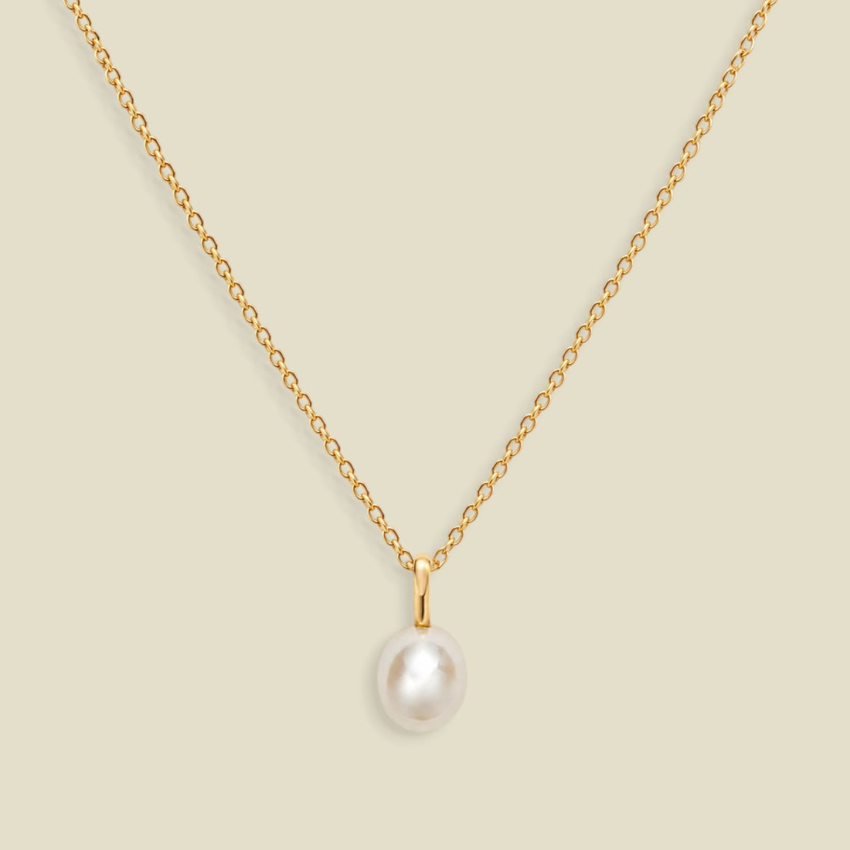 A gold dainty pendant necklace with a freshwater pearl charm, set on a solid soft beige background
