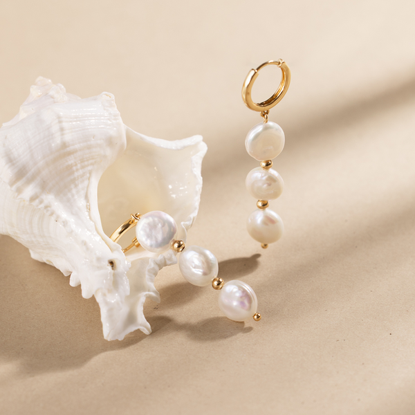 Gold hoop earrings with three dangling pearls next to a white seashell.