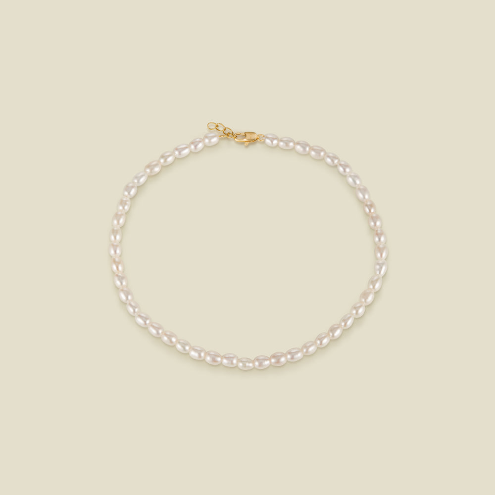 A pearl strand anklet with a gold lobster clasp and extender, set against a solid beige background.