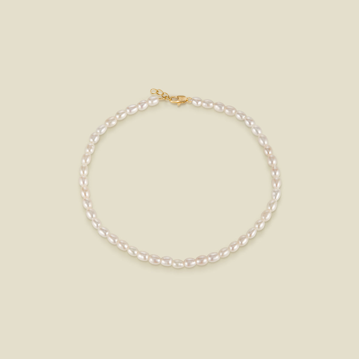 A pearl strand anklet with a gold lobster clasp and extender, set against a solid beige background.