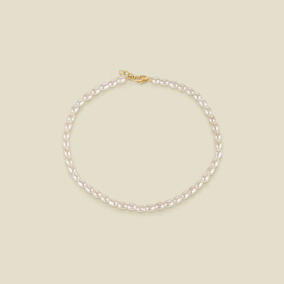 A pearl strand anklet with a gold lobster clasp and extender, set against a solid beige background.
