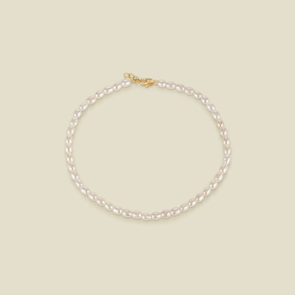 A pearl strand anklet with a gold lobster clasp and extender, set against a solid beige background.