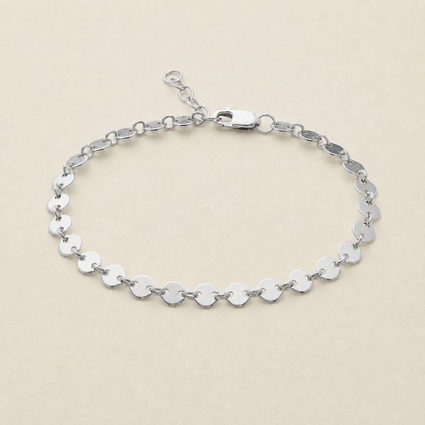 A silver chain bracelet made of flat, polished oval links, displayed on a light beige background.