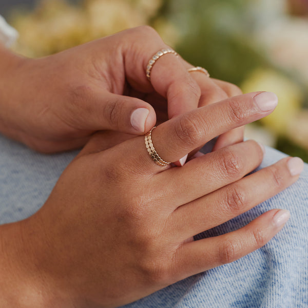 Close-up of hands wearing delicate textured gold rings, resting on light blue denim.