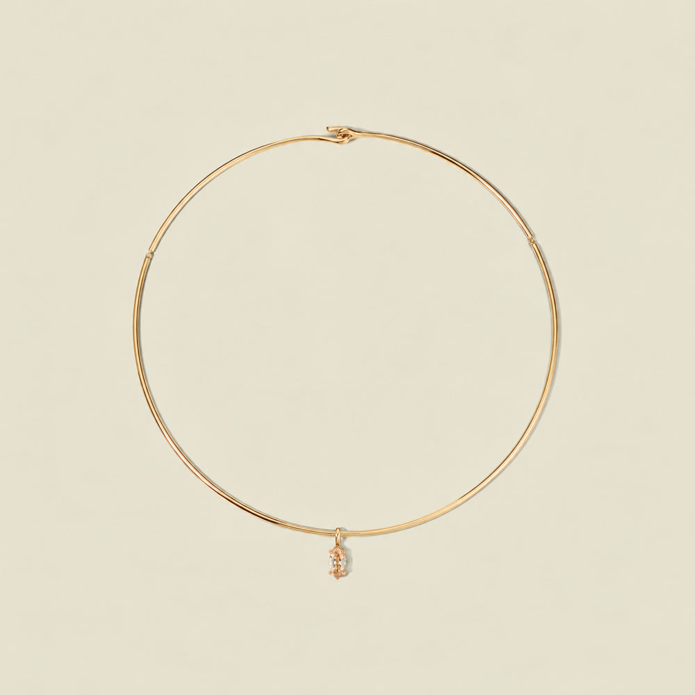 A thin gold wire hoop necklace with a small dangling golden yellow marquise gemstone pendant, displayed on a solid light beige background.
