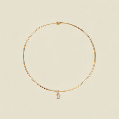A thin gold wire hoop necklace with a small dangling golden yellow marquise gemstone pendant, displayed on a solid light beige background.