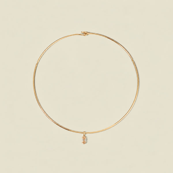 A thin gold wire hoop necklace with a small dangling golden yellow marquise gemstone pendant, displayed on a solid light beige background.