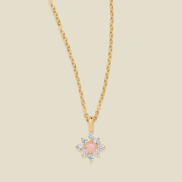 Gold chain with a pink prong-set pendant against a neutral backdrop.