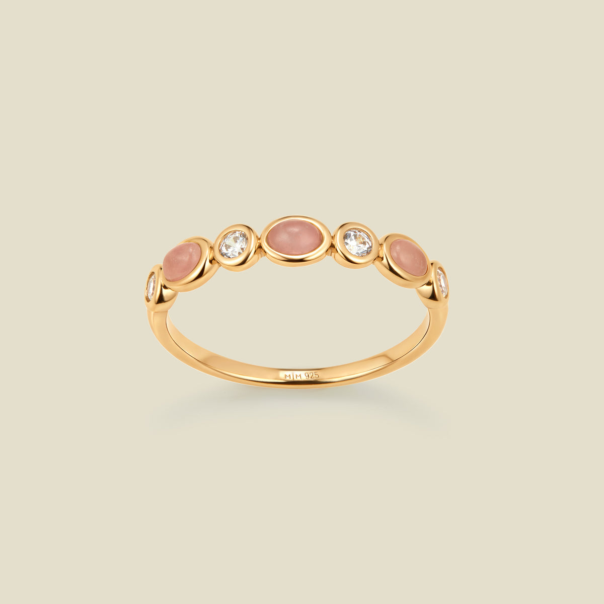 Gold ring with bezel-set pink and clear stones against a neutral background.