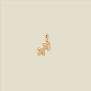 A gold pendant shaped like the Sagittarius zodiac symbol, featuring two small clear gemstones, centered on a solid light beige background.