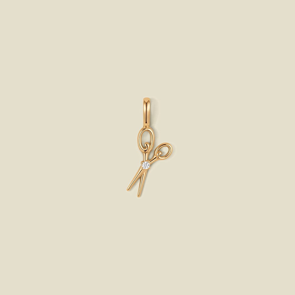 A gold scissor pendant charm with a small clear stone in the center.