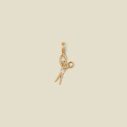 A gold scissor pendant charm with a small clear stone in the center.