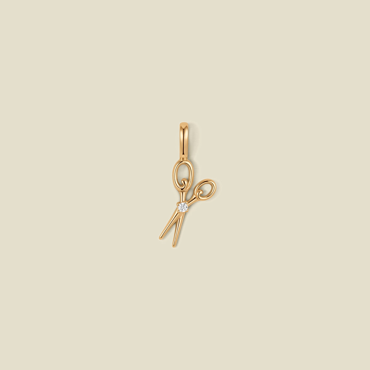 A gold scissor pendant charm with a small clear stone in the center.