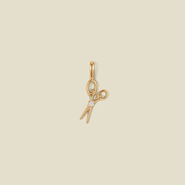 A gold scissor pendant charm with a small clear stone in the center.