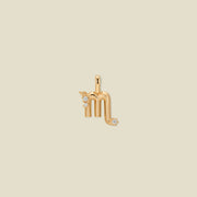 A gold pendant shaped like the Scorpio zodiac symbol, featuring three small clear gemstones, centered on a solid light beige background.