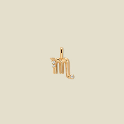 A gold pendant shaped like the Scorpio zodiac symbol, featuring three small clear gemstones, centered on a solid light beige background.