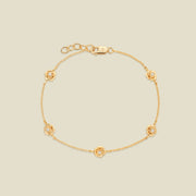 A delicate gold chain bracelet featuring five ornate, textured gold peony charms with small clear stones, arranged in a circle on a light beige background.
