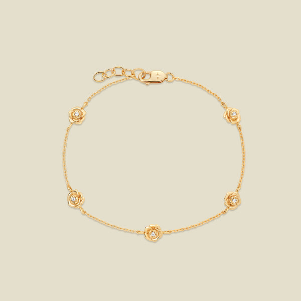 A delicate gold chain bracelet featuring five ornate, textured gold peony charms with small clear stones, arranged in a circle on a light beige background.