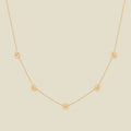 A delicate gold chain necklace featuring five small, evenly spaced textured peony flower motifs set with tiny clear stones, displayed on a solid light beige background.
