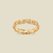 A gold floral-etched ring band with peony flowers and small clear gemstones, shown on a plain warm beige background. 